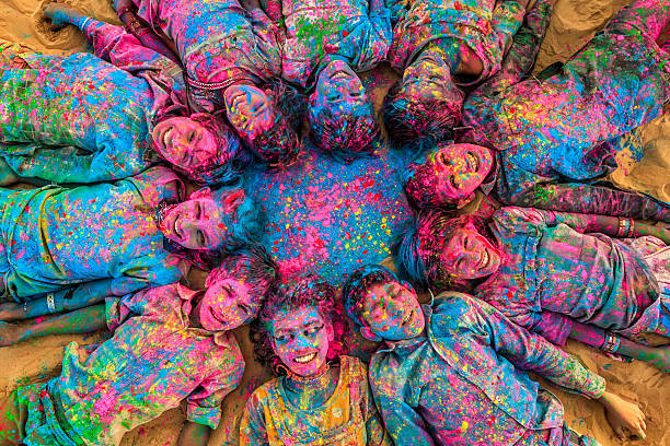 Group of happy Gypsy Indian children playing happy holi on sand dunes in desert village, Thar Desert, Rajasthan, India. Children are lying in a circle. Color powders are on their faces and clothes. Holi is a religious festival in India, celebrated, with the color powders, during the spring. istockphoto 522121310 612x612